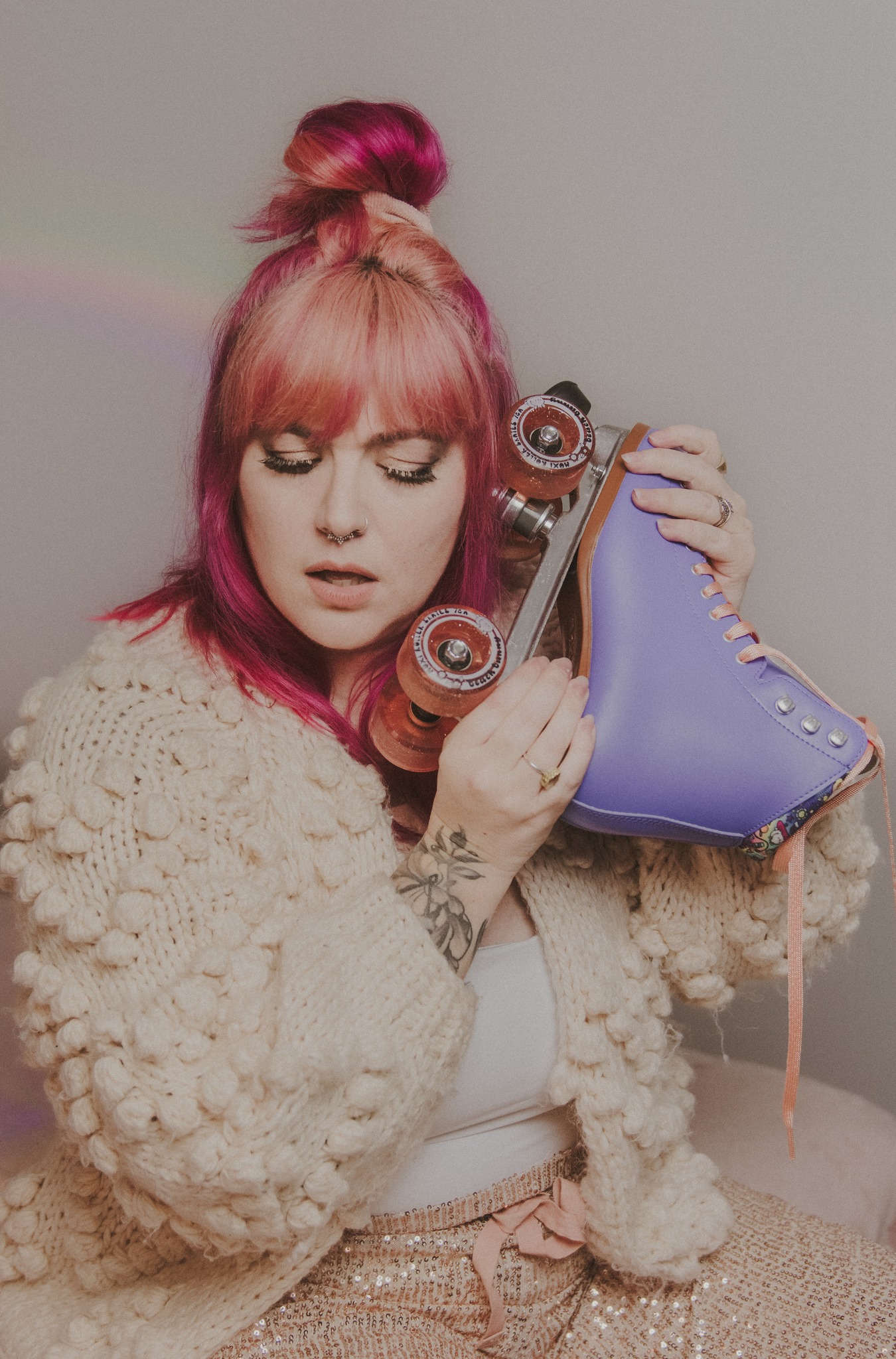 Grace, with pink hair in a fluffy cream sweater, holds a purple roller skate up to her ear like a phone.